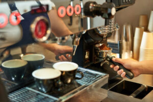 Close-up of a barista's hand holding a portafilter filled with fresh grounds at an espresso machine for wholesale Ethiopian coffee UK.