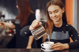 A smiling barista pouring steamed milk into a white cup, perfect for wholesale Ethiopian coffee UK cafe service.