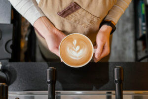 Top-down view of a barista holding a cup of coffee with detailed floral latte art, representing premium wholesale Ethiopian coffee UK.